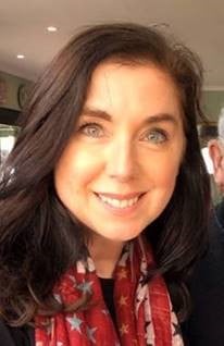 A woman with brown hair smiles at the camera. She is wearing a red scarf.