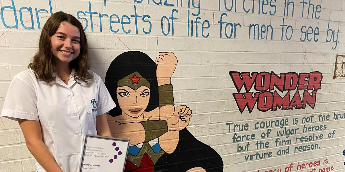 Student holding a certificate in front of a mural